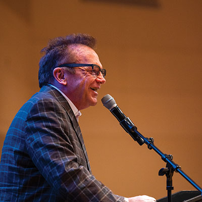 Tom Arnold speaks on stage at a podium during the annual Conference on Addiction held by UVU’s College of Humanities and Social Sciences in March 2023.