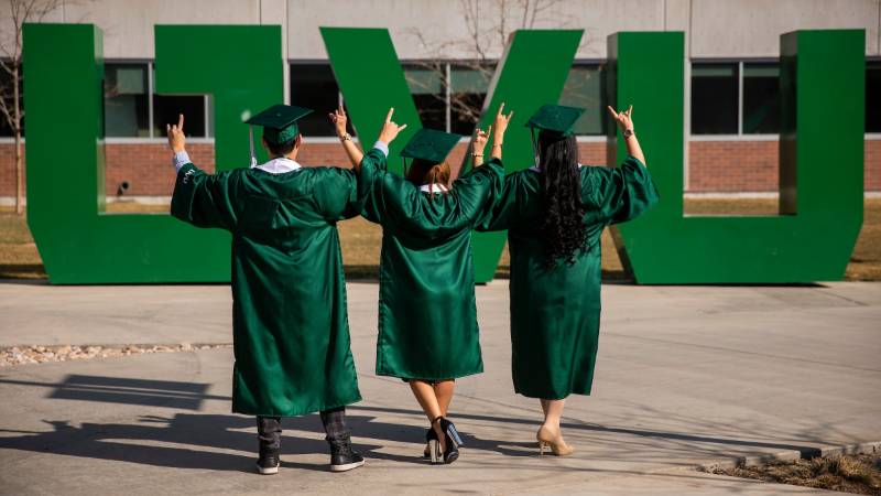 Graduates standing in front of the UVU sign