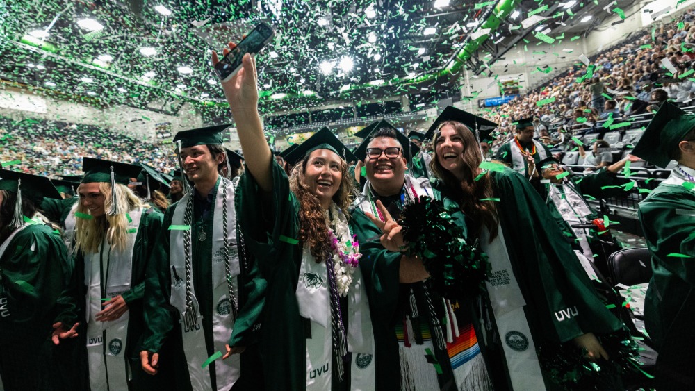 A group of UVU graduates in graduation regalia celebrate at commencement.