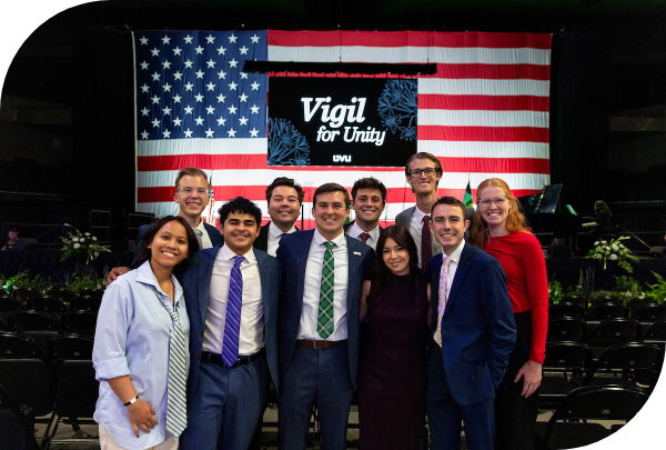 Ten students standing in front of a large american flag and a sign that says Vigil for Unity