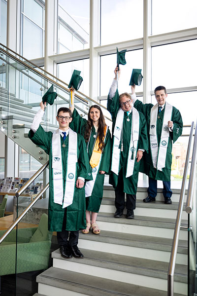 4 Graduates holding their caps on a staircase