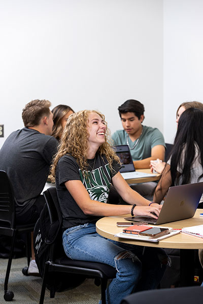 Photo of people in a class, focused on a women and her laptop