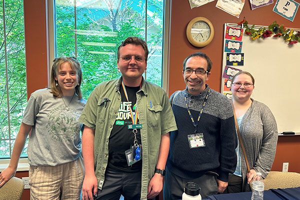 4 people lined up posing for a picture in a classroom