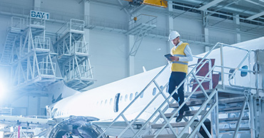 Worker in safety uniform walking down steps in an airplane hanger