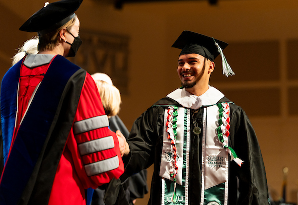 Social Work Graduate holding shaking hands with faculty during graduation on stage