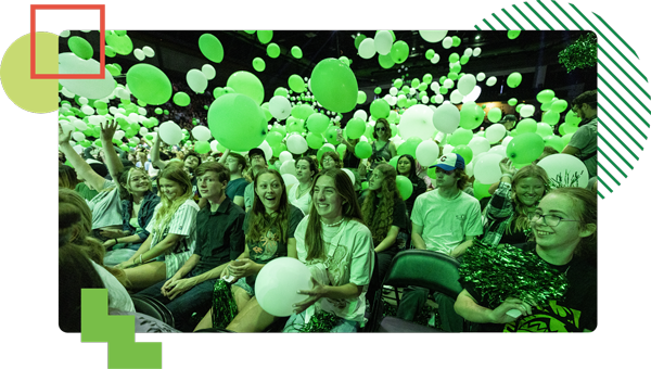 UVU Students bathed in green light with green balloons dropping on them