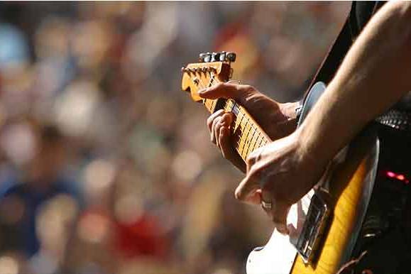Image of a person's hands playing guitar in front of a crowd