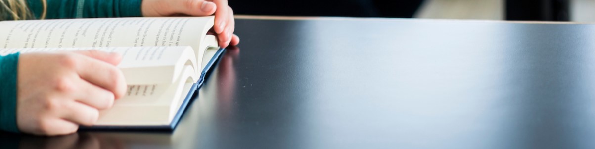 Hands holding open text book on a black table.