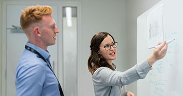 two people writing on a white board