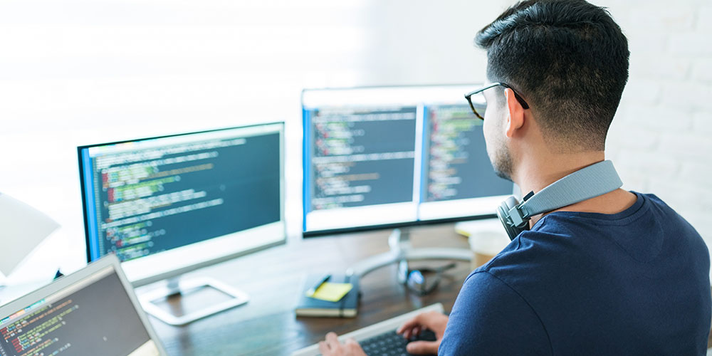 man using several computer monitors with code