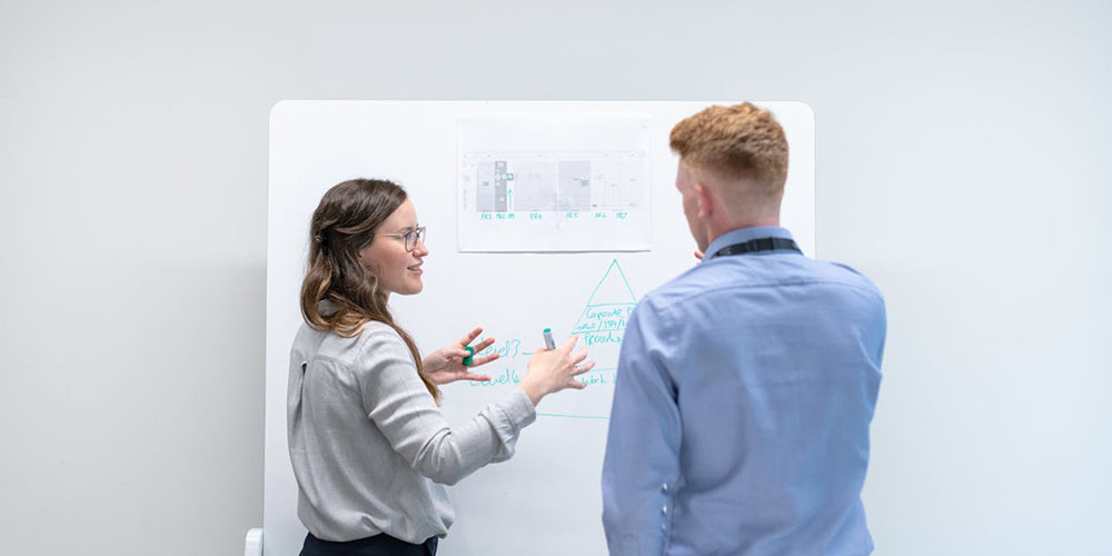 two people standing in front of a whiteboard