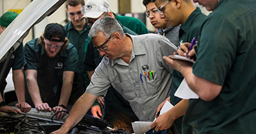 man teaching students how to fix a car