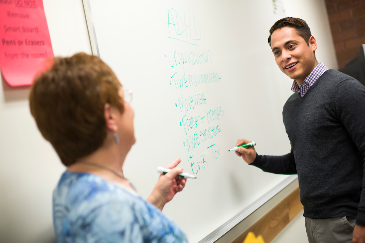 Teacher with student at the front of the classroom on a whiteboard.