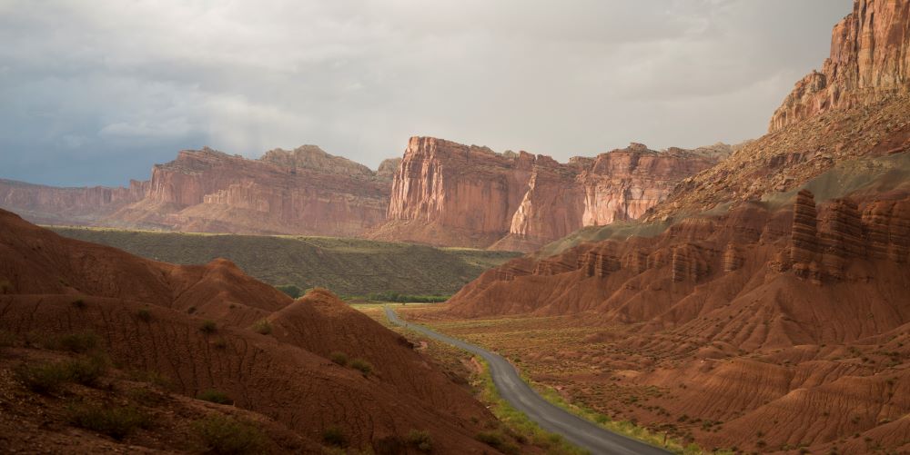 The Scenic Drive cuts through the Moenkopi Formation in the foreground, on both sides of the road. On the right, above the Moenkopi is the gray Chinle Formation. In the distance rise the sheer Wingate Cliffs