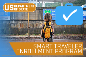 US State Department - Smart Traveler Enrollment Program. Image of Person with backpack on standing in front of sign in a foreign language