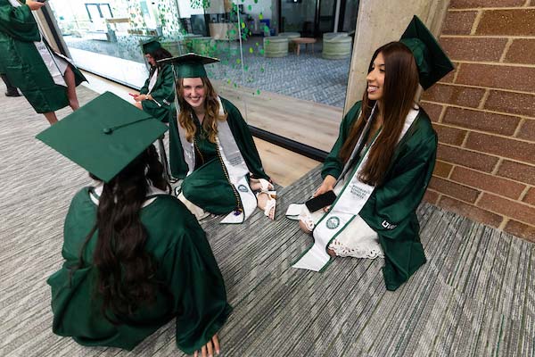 UVU Graduates sitting on the floor dressed in UVU graduate attire