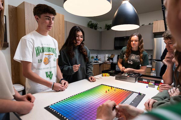 A group of students standing around a kitchen island working on a puzzle together.