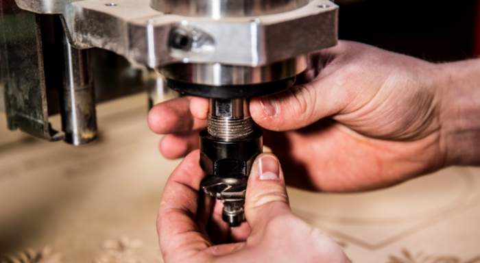 A Drill press drilling through a piece of wood.