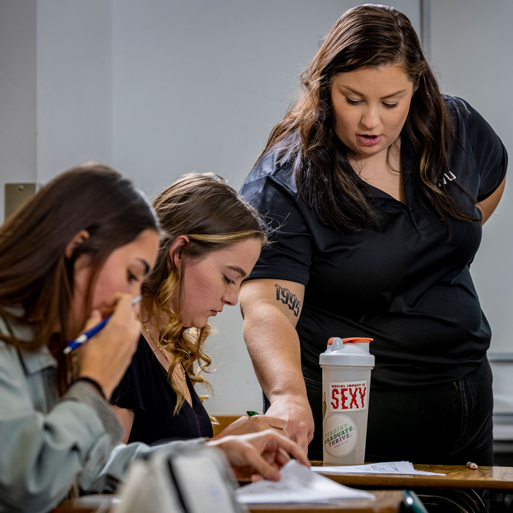 Female teacher helping 2 female students with work at their desks