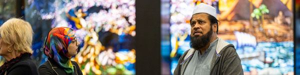 An Interfaith Student Council event with a diversity of religions represented by the people standing in front of the Roots of Knowledge stained-glass exhibit at UVU