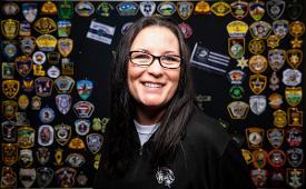Bobbi Kassel poses in front of a wall of service patches.