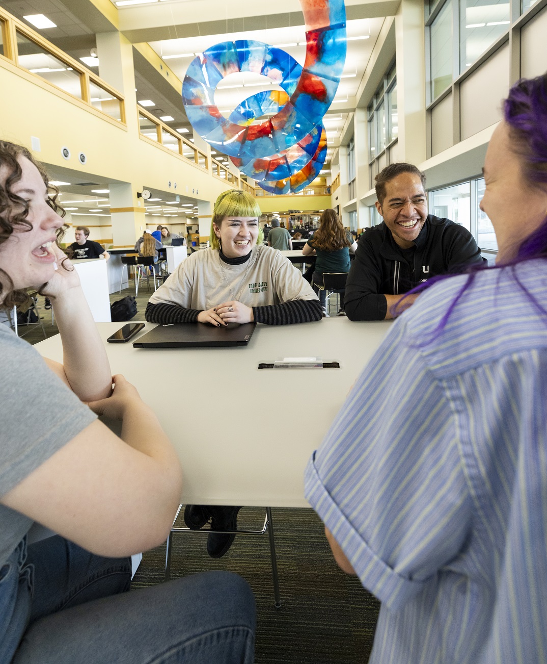 Four UVU students laugh together while at a table in the Fulton Library.