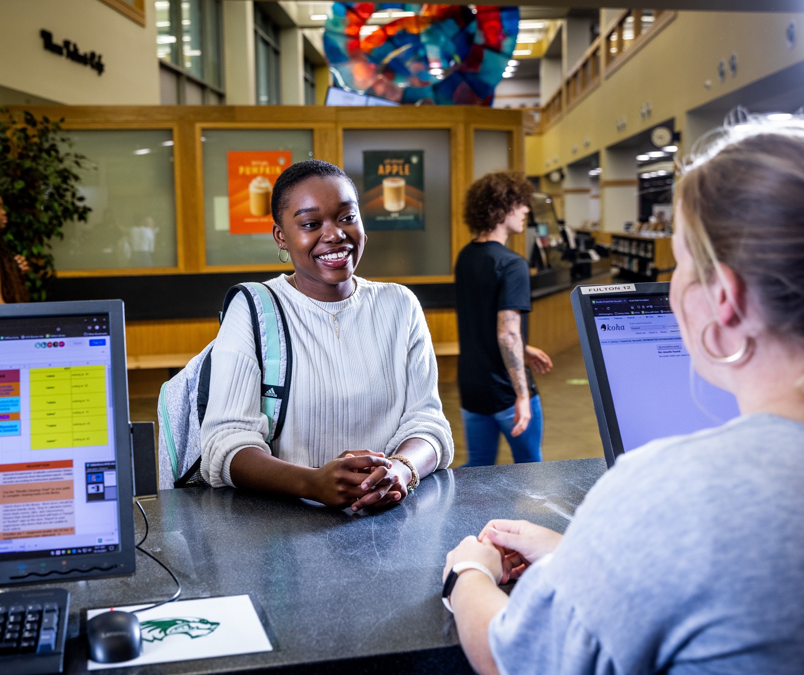 A UVU student discusses equipment checkout with a library aide at the Fulton Library Circulation Desk.