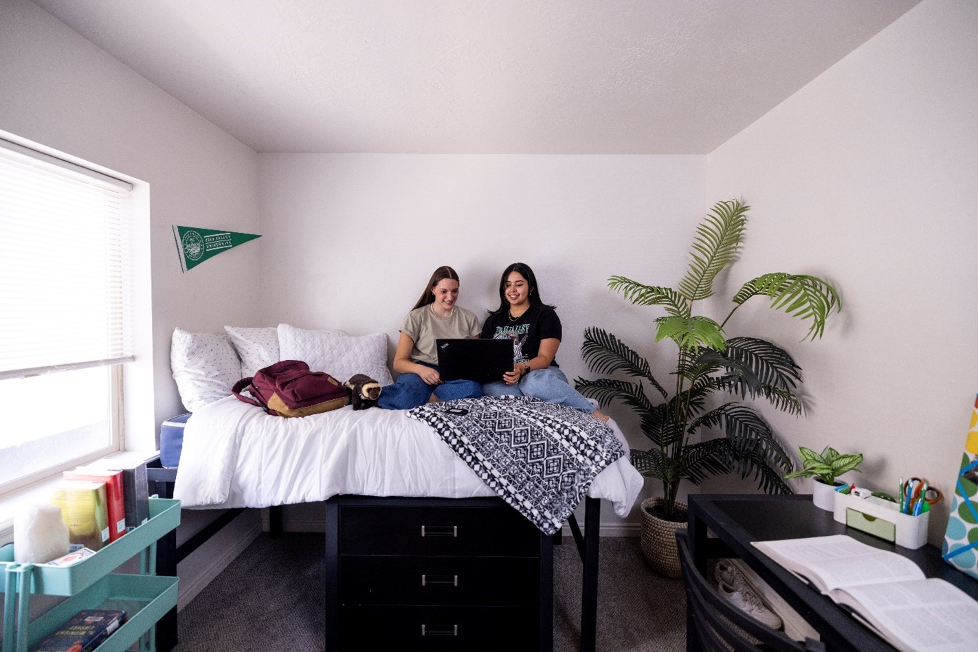 Two UVU students in a dorm room, on a bed, looking at a laptop.