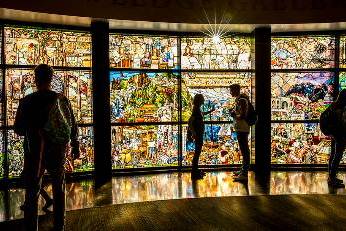 light shines through the stained glass windows of the roots of knowledge exhibit, casting those in the room looking at it as silhouettes