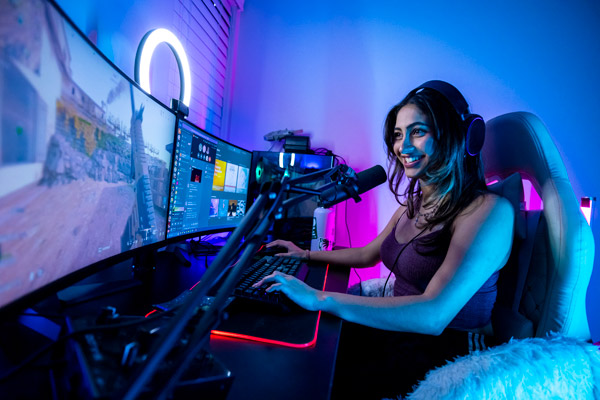 A woman sitting a her computer, with a gaming setup, pleaying video games.