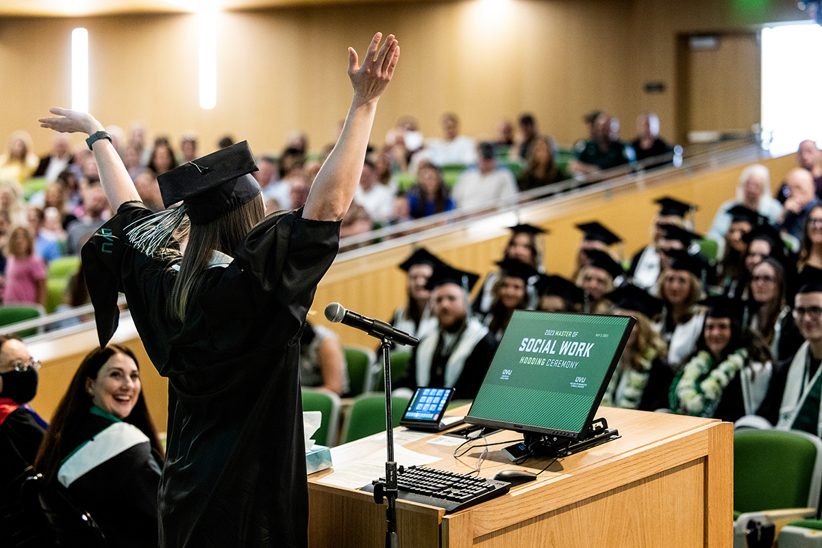 a graduating student giving a speech with their arms up celebrating