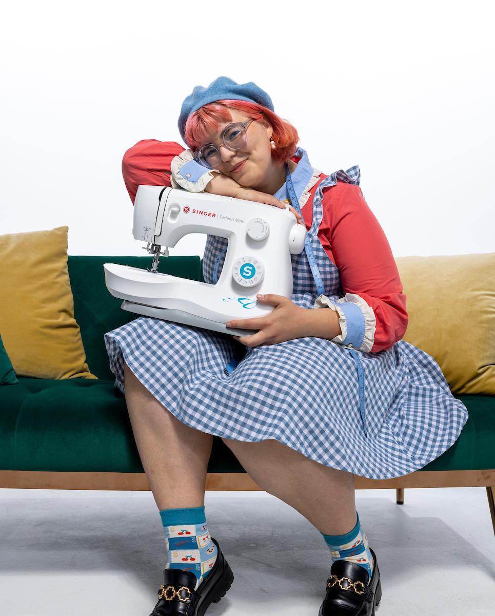 Veronica Clark sitting on a green couch, smiling, holding a sewing machine