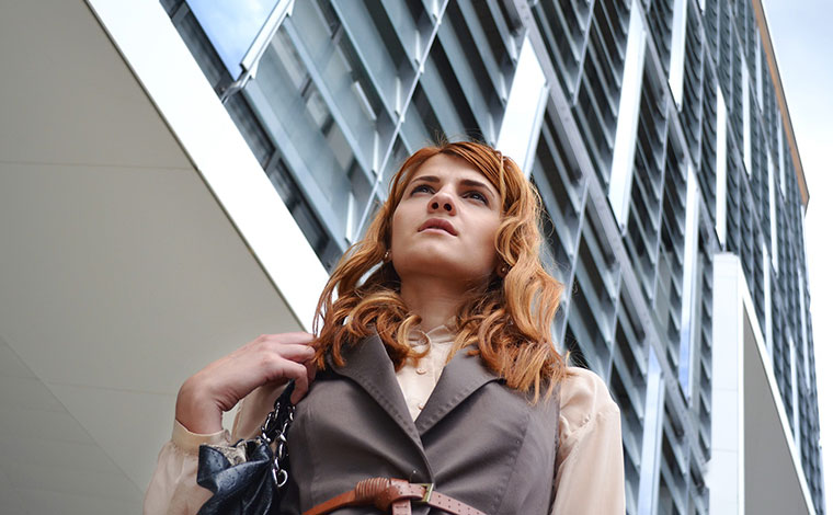 Woman walking with a tall building in the background.