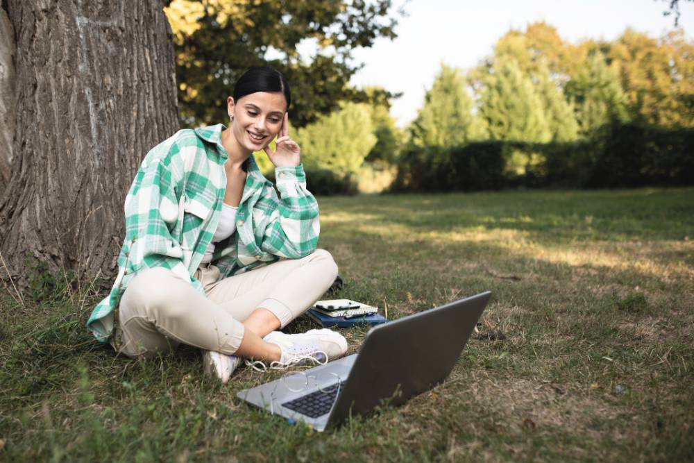 Student viewing their laptop under a tree