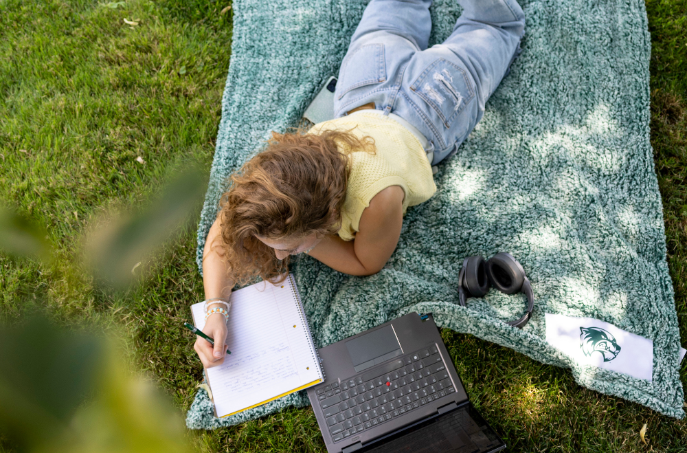 Student writing notes with a laptop in front of them