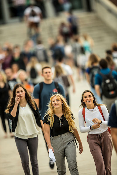Three female students walking around UVU campus with other students in the background.