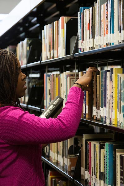 A woman looking through a shelf of books in a library.