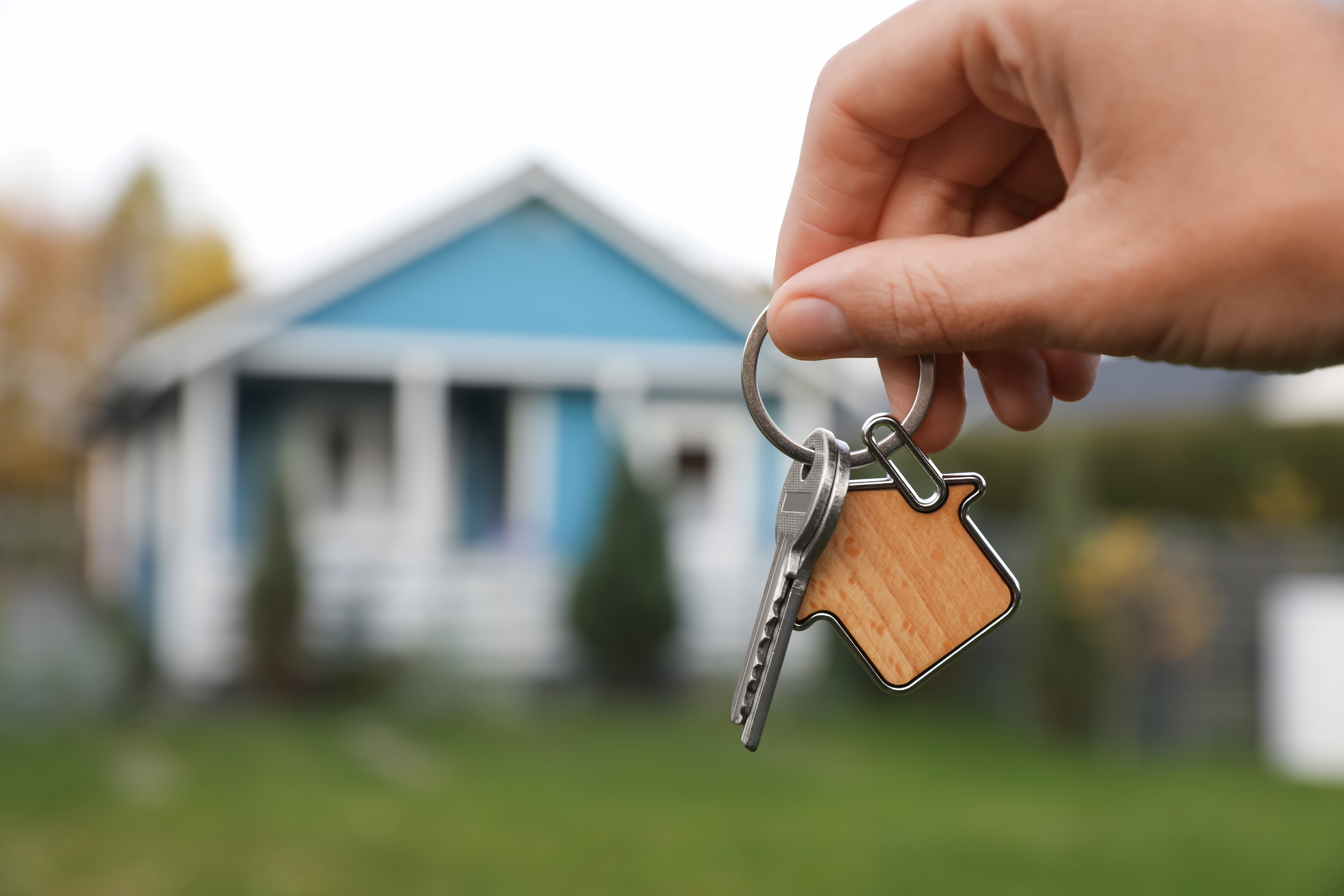 Keys in focus being held in front of a blurry home