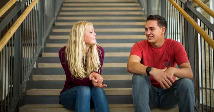 Two students sitting on a set of stairs talking to one another.