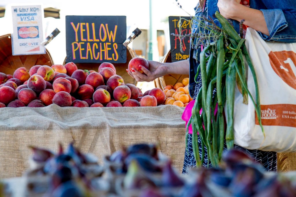 SHopper shopping at a farmers market, looking at a pile of fruit