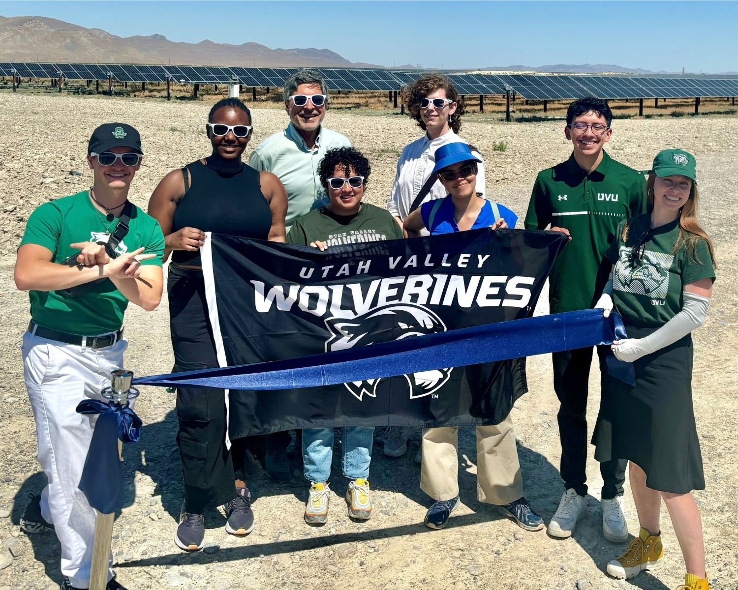 A group of people from UVU holding a UVU flag with the Elektron Solar farm in the background