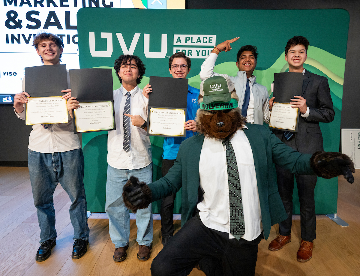 Group of students excited in front of green backdrop with UVU logo