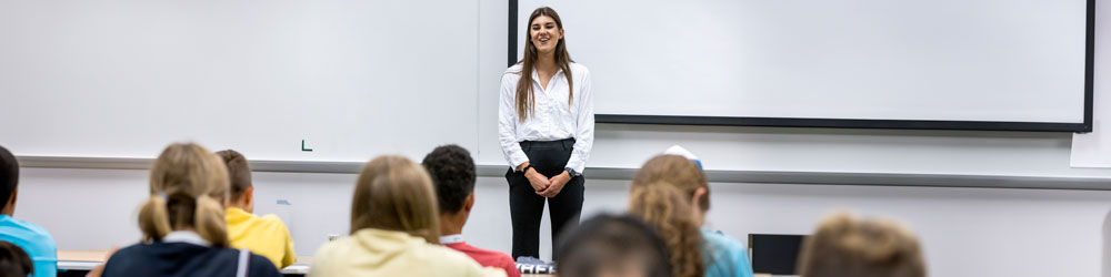 A woman talking at the front of a classroom full of students