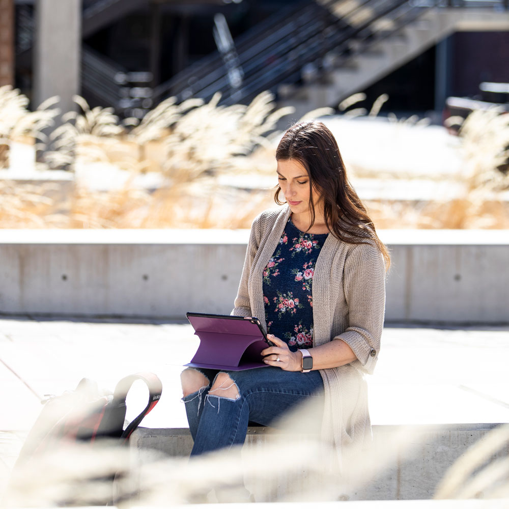 female student sitting outside on UVU campus working on tablet